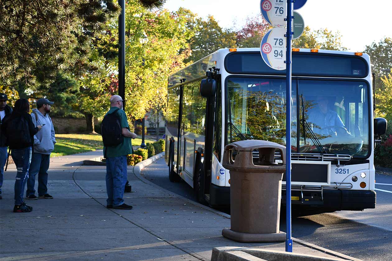 Rider with phone in hand waving as bus approaches stop. Stop sign/amenities, bus overhead sign, operator visible